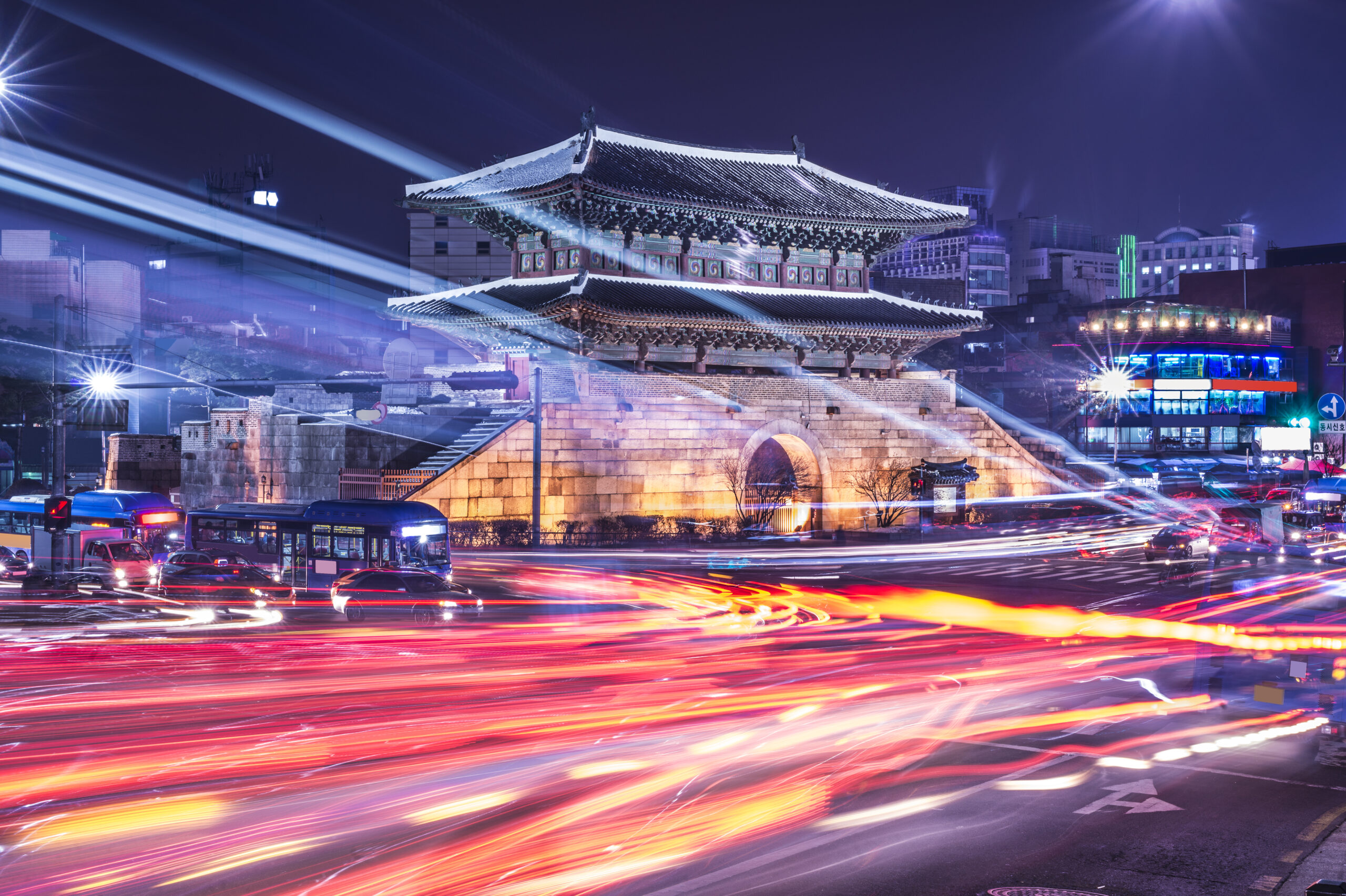 Night view of a bustling cityscape in Seoul, South Korea, featuring the illuminated Namdaemun Gate surrounded by vibrant streaks of city traffic lights, symbolizing the dynamic energy of marketing and connectivity in Asia.